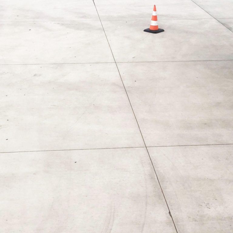 Smooth light colored concrete floor with orange striped cone